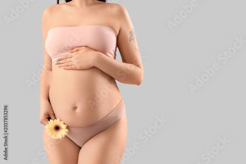Young pregnant woman in underwear with gerbera flower on light background
