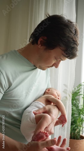 Loving father carefully cradles his sleeping newborn son in his arms, rocking him gently by the window, cherishing a heartwarming moment of bonding, care, and family connection