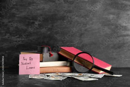 Tableau sur toile Paper with text PAY OFF STUDENT LOANS, magnifier, books and money on dark table