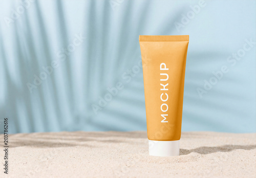 Yellow cosmetic cream tube mockup standing on a sandy beach with tropical palm leaf shadow on a light blue background