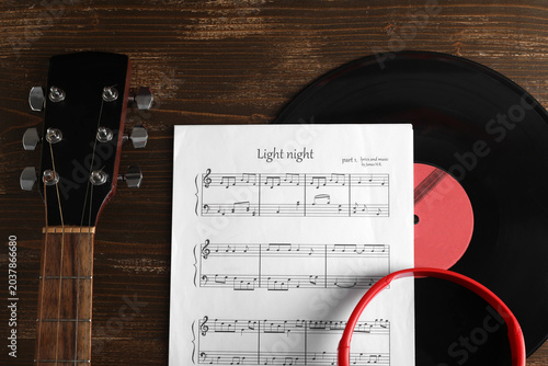 Music sheet, vinyl disk, headphones and guitar on wooden background, closeup