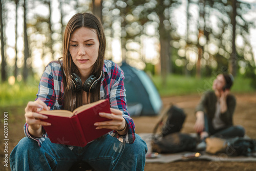 Tableau sur toile Woman reading book at campsite relaxing in nature