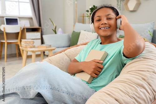 African-American teenage girl in headphones listening to audiobook with book ...