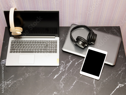 top view of two laptops with headphones and a tablet lying on a dark marble countertop