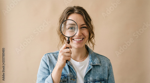 Young woman holding magnifying glass playfully over her eye, smi