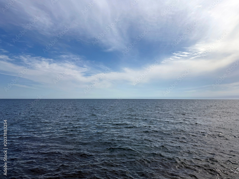 Fototapeta premium Open sea with calm blue water and sky clouds.