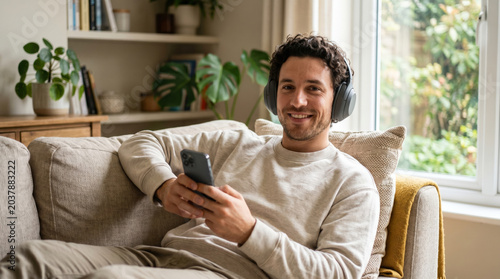 Relaxed man wearing headphones smiles while holding a phone on a