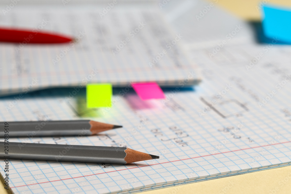 Naklejka premium Copybook with handwritten maths formulas with pencils on yellow background, closeup