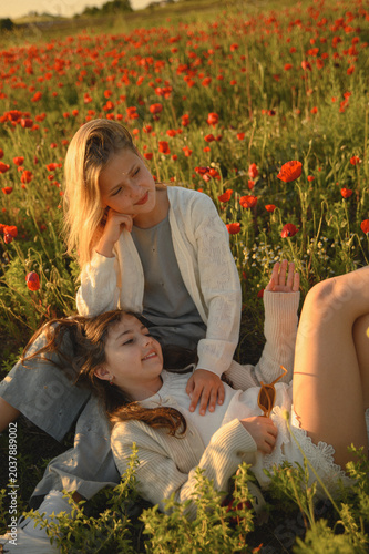 Two little girls laughing and hugging in blooming poppy field, playful childhood friendship moment filled with joy, warmth and carefree summer atmosphere