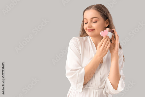 Beautiful young woman with heart-shaped sponge and cream on light background