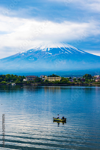 Two unidentifiable persons fishing from boat on Lake Kawaguchiko with clouds descending on snow-covered Mt Fuji in background