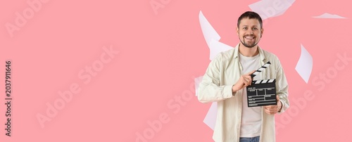 Fotografie Male actor with movie clapper and falling papers on pink background with space f
