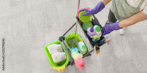 Foto Female janitor with trolley of cleaning supplies in room, top view