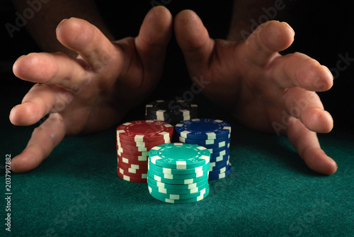 Tableau sur toile Two hands hover over a collection of poker chips in various colors stacked on a green felt surface