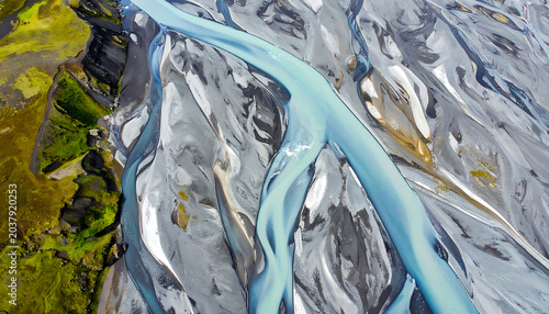 Aerial view of a braided river delta with vibrant blue water flowing through gray gravel beds and green mossy banks, natural landscape pattern