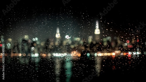 雨の窓ガラスに付いた水滴と夜景のぼやけた街並み。都市の夜の雰囲気や背景素材に適した風景