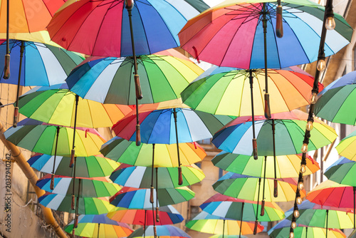 Creative street decoration featuring dozens of colorful hanging umbrellas suspended above a narrow urban street in Bucharest