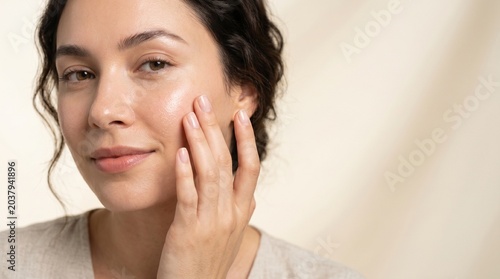 Woman applying skincare product to her glowing face with soft natural light