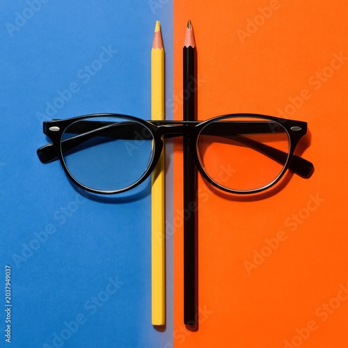 Colored Pencils and Glasses Arranged on Blue and Orange Background in Creativ...