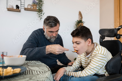 Photos Father feeding son with cerebral palsy in wheelchair