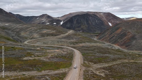Aerial view of winding mountain road and valley in Russia, Chukotka, Provideniya. Slow pan follows the S-curve across tundra slopes. Wide establishing frame with tiny vehicle on the track