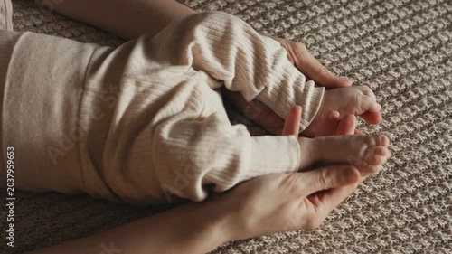 Mother gently touching moving legs of baby lying on blanket