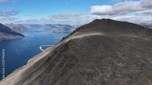Drone establishing shot of rocky ridgeline above Provideniya Bay, Russia, Chukotka. Wide master shot on a steady side follow, showing arctic slopes and shoreline in daylight