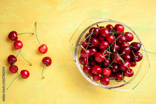Fresh ripe red cherries in a transparent glass bowl on a yellow wooden table. sweet summer berry, organic food background
