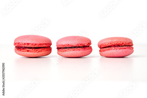 Three fresh pink macarons with dark berry filling arranged in a row on a white background. sweet french confection
