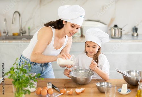 Photos Happy mother and her daughter adding flour in bowl and whisking ingredients usin