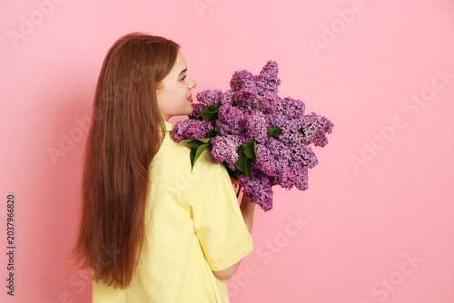 Teenage girl with bouquet of lilac flowers on pink background, space for text