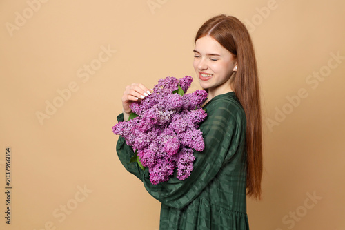 Teenage girl with bouquet of lilac flowers on beige background, space for text