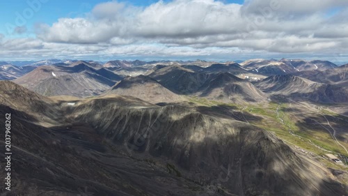 Aerial view across endless ridges with slow horizontal pan. Rugged tundra valleys under daylight clouds, Russia, Chukotka, Provideniya. Scenic nature background for exploration and travel