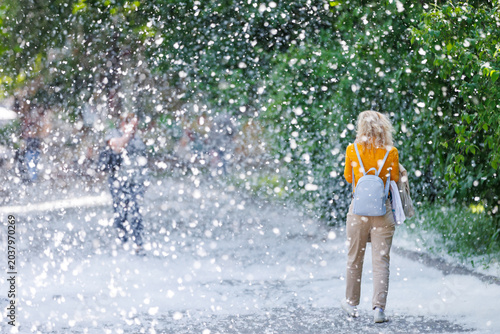 Foto Unrecognizable woman walking through a massive poplar fluff storm in a city park
