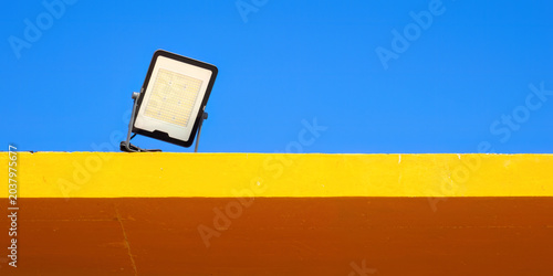 Modern LED floodlight above colorful wall against clear blue sky in minimalist architectural composition