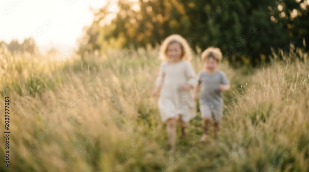 Fototapeta premium Children run joyfully through a tall grass field during the golden hour while exploring the beauty of nature in the countryside.