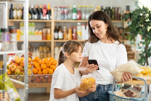 Mother and daughter checks expiration date of cornflakes and oat flakes - scans QR code on label with smartphone