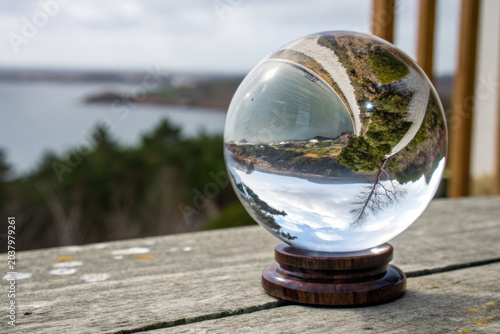 Crystal ball glass sphere wooden base landscape reflection outdoor scene nature view inverted image clear sky water body green trees wooden