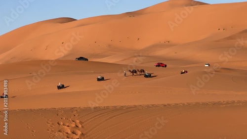 Camel caravan crossing Sahara dunes alongside modern desert adventure tourism