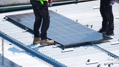 Two worker installing solar panel on metal roof at construction work site