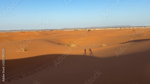 Long human shadows stretching across Sahara sand dunes at golden hour
