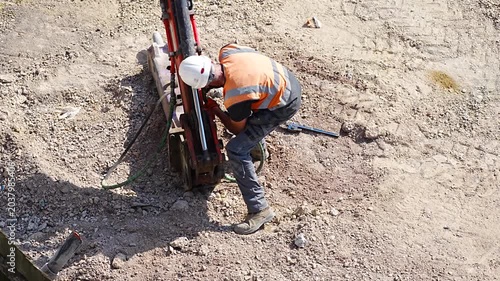 Worker in orange vest operating drill machine at outdoor excavation work site