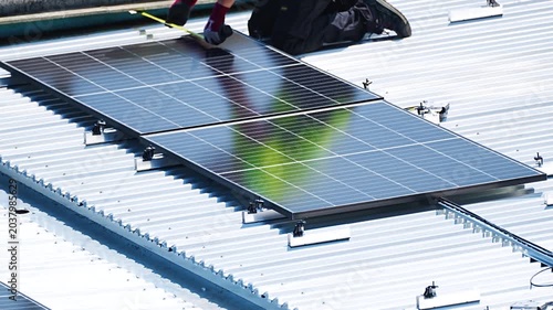 Worker installing and securing large solar panel on corrugated metal rooftop