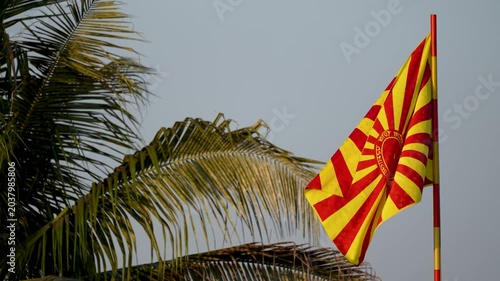 Yellow and red striped flag waving on pole beside swaying palm tree