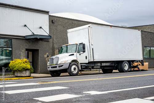 Popular day cab middle duty rig semi truck with long box trailer unloading cargo standing on the city street