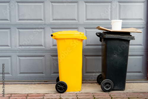 Quadro su tela yellow and black recycling bins in front of garage door
