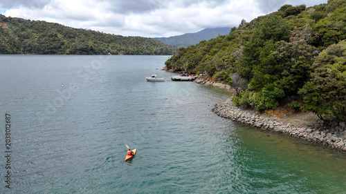 Aerial view of kayaker paddling in sheltered coastal bay surrounded by forested hills