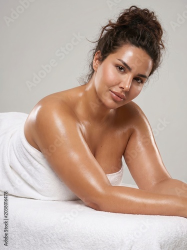 A beautiful woman with naturally glowing, healthy skin, wrapped in a plush white towel, enjoys a tranquil moment of luxurious pampering and self-care at a spa for ultimate relaxation and rejuvenation