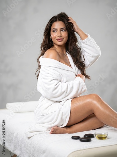 Elegant woman in white robe lounging on bed with relaxed pose and soft spa atmosphere