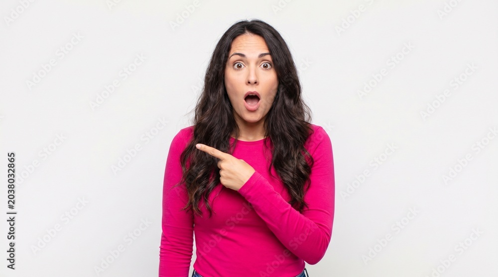 Naklejka premium Surprised Young Woman Pointing to the Side Against White Background
